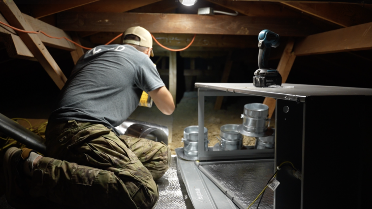 HVAC technician sealing ductwork connections inside an attic during a ventilation system installation.
